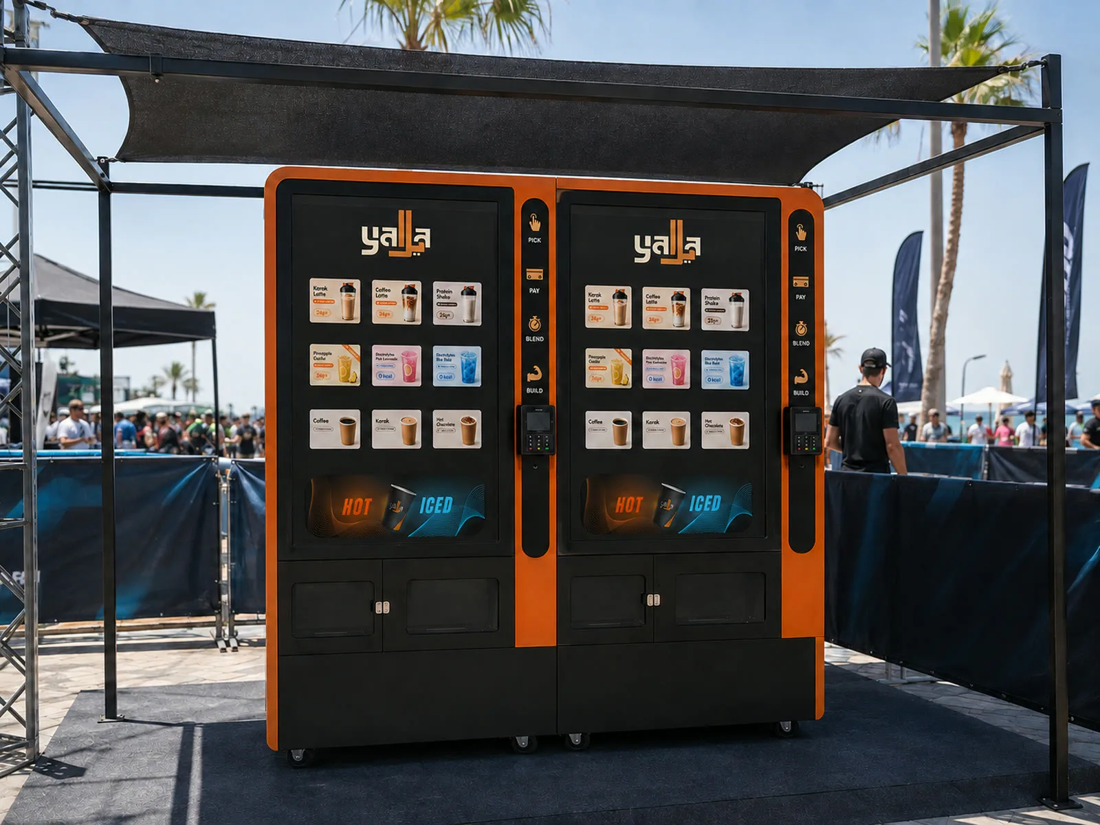 Two Yalla machines under a shade canopy at a beachfront event with crowds behind